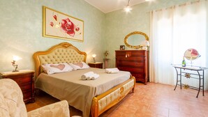 A bedroom with a bed, a dresser, a vanity with a mirror, and a painting on the wall.