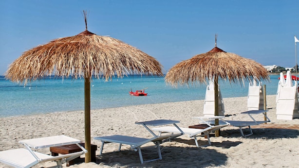 Ein Strand mit Strandkörben, Liegestühlen und einem klaren, blauen Meer.