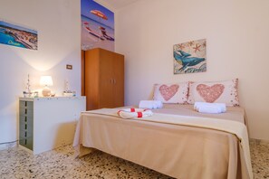 A bedroom with a bed, a wardrobe, a desk with a lamp, and a wall with a painting.