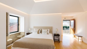 A bedroom with a large bed, a window with a view, a bench, and a door leading to an outdoor area. - Casa Vieira Lobo (Arouca)