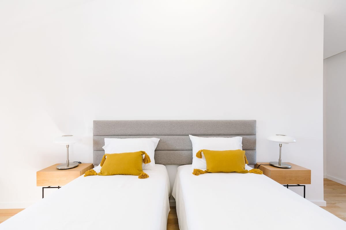 A double bed with white bedding and two mustard-colored pillows, flanked by nightstands with lamps.
