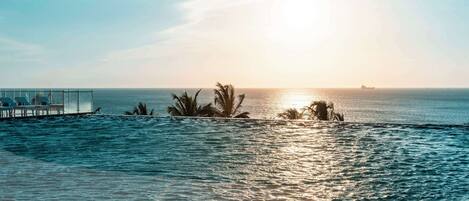 A waterfront hotel with a pool, palm trees, and a sunset view.