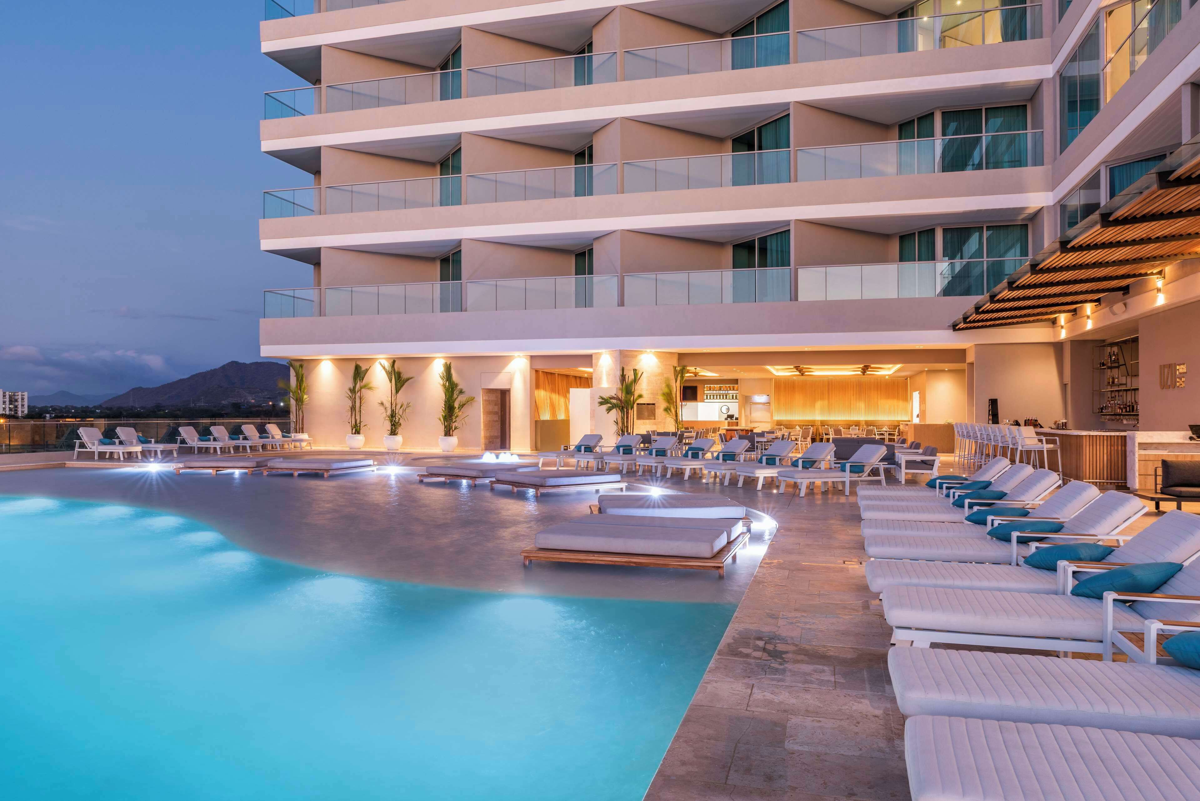 A hotel with a pool area, lounge chairs, and a bar.