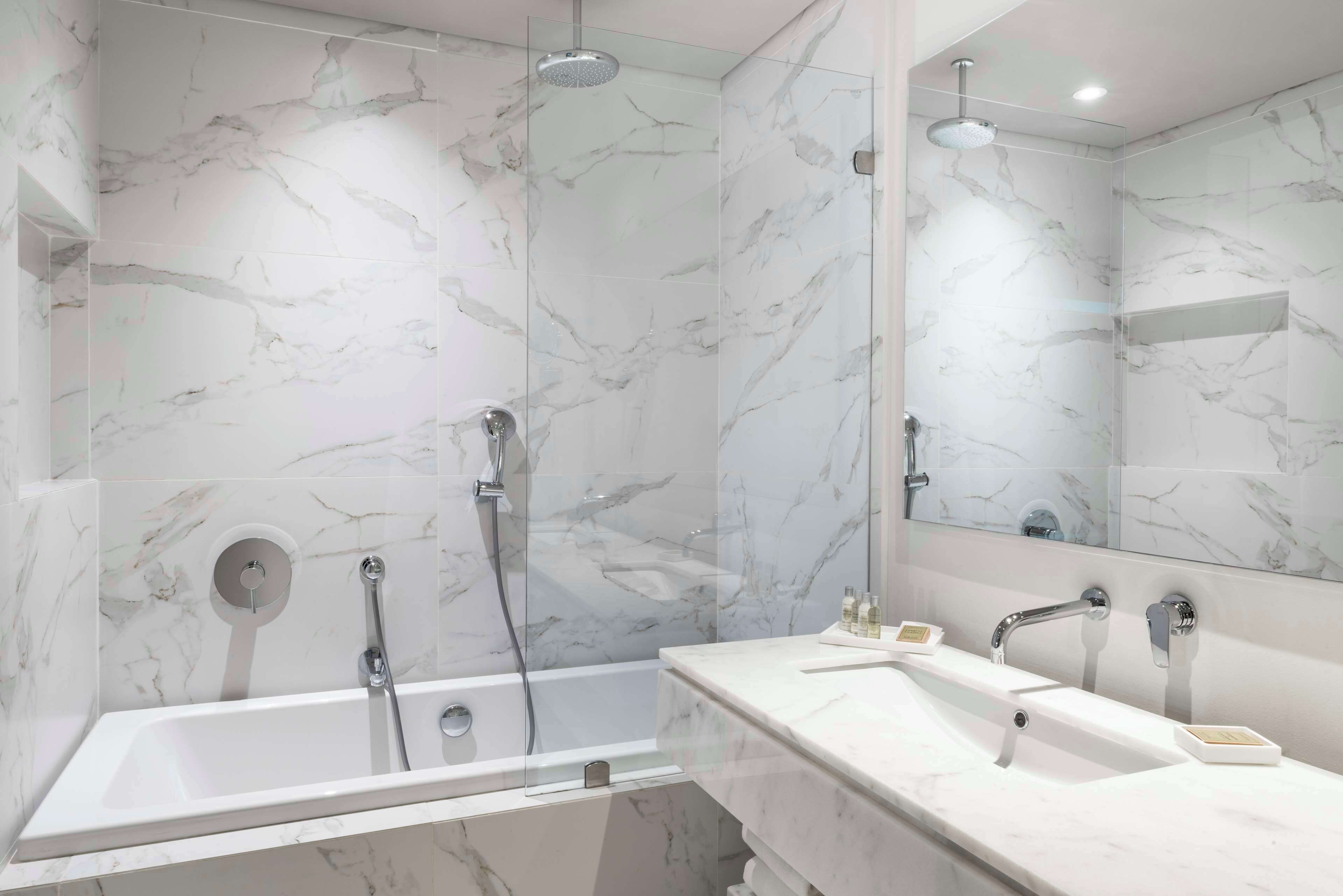 Un baño moderno con pared de mármol, ducha con cerramiento de vidrio y tocador doble.