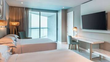 A modern hotel room with two beds, a desk, a TV, and a large window with curtains.