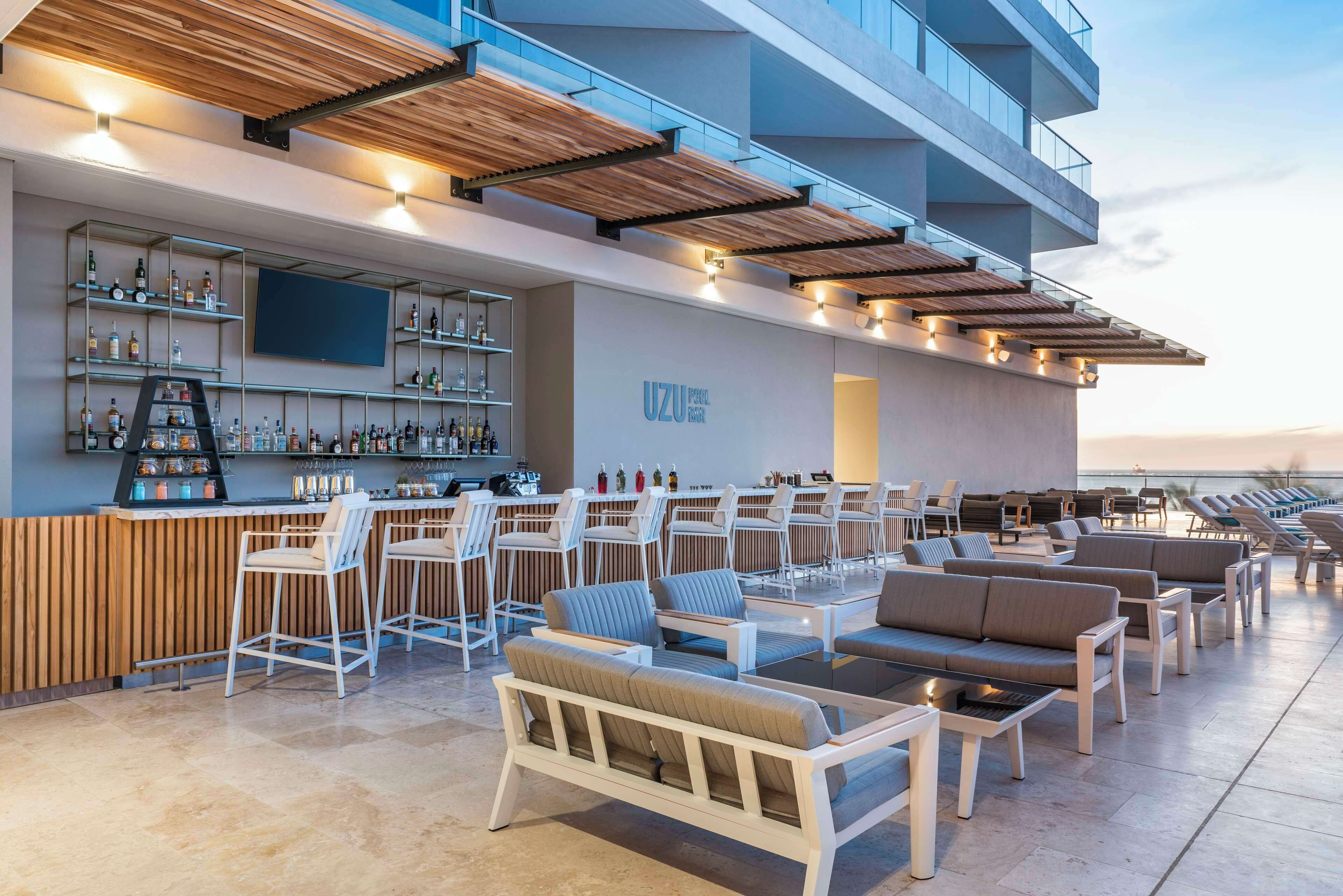 Un bar situé sur le toit, avec des tabourets, des espaces pour s’asseoir et un grand écran.