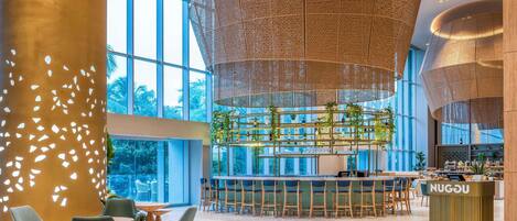 A spacious lobby with a bar area, large windows, and a modern chandelier.