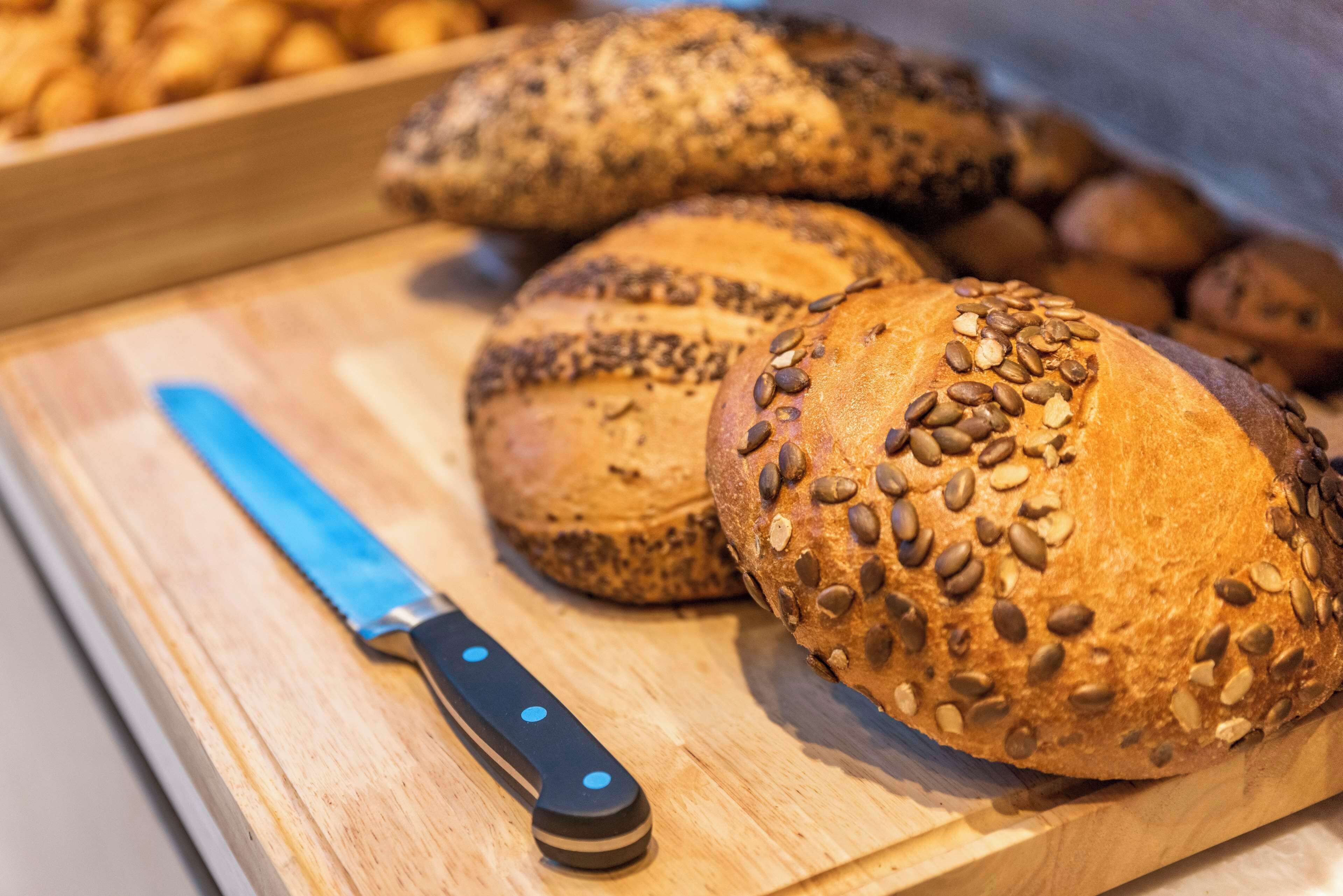 A wooden cutting board with several loaves of bread, some topped with seeds, and a knife with a blue handle.