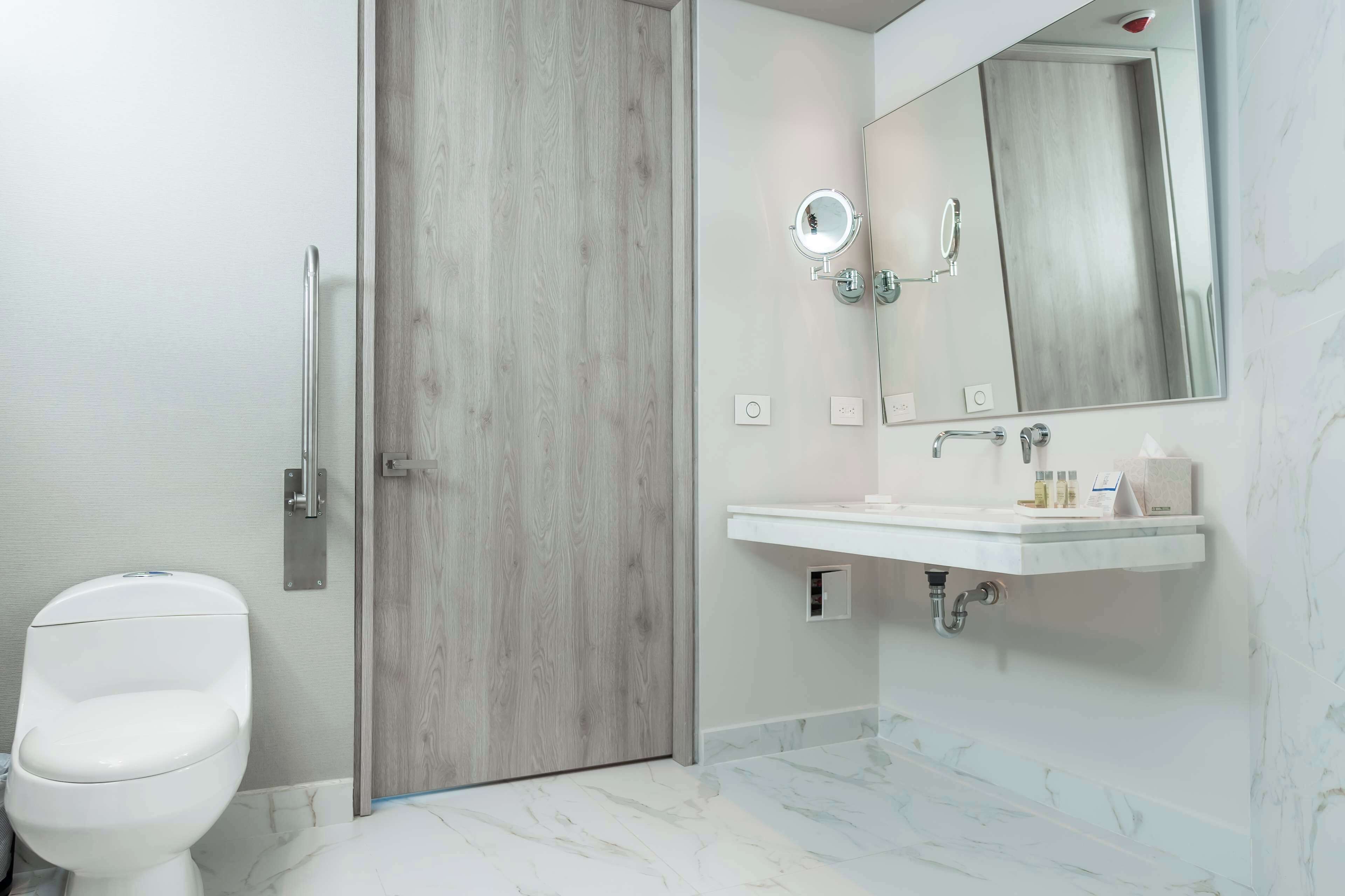 Un baño moderno con puerta de madera, inodoro blanco, lavabo con espejo y suelo de mármol.