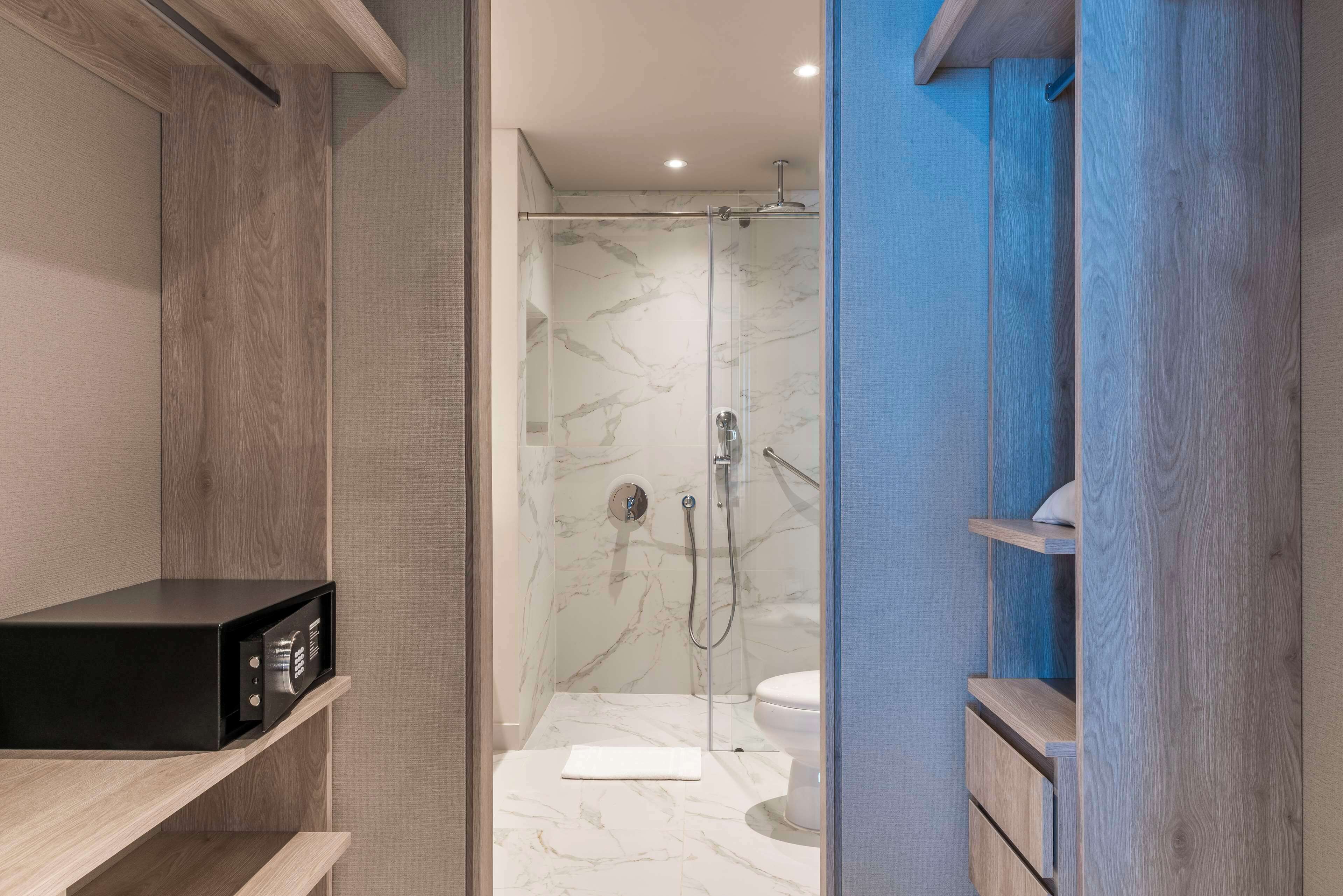 A modern bathroom with a shower, a toilet, and a black appliance on a shelf.