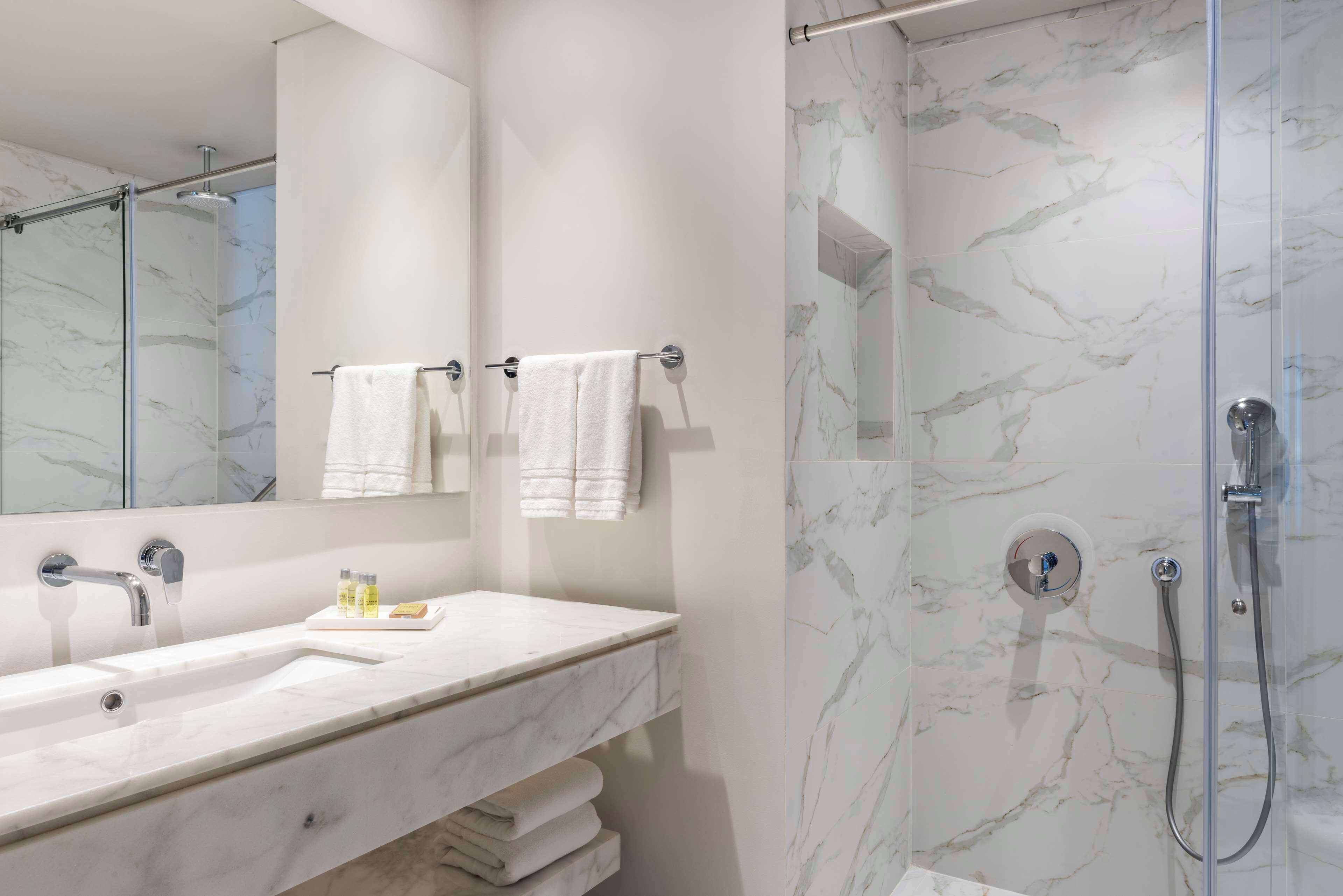 A modern bathroom with a marble sink, a glass-enclosed shower, and two towels hanging on hooks.