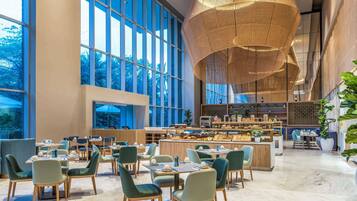 Un vaste espace dédié à la salle à manger, doté de hauts plafonds, de grandes fenêtres et d’un comptoir central où sont présentés les plats.