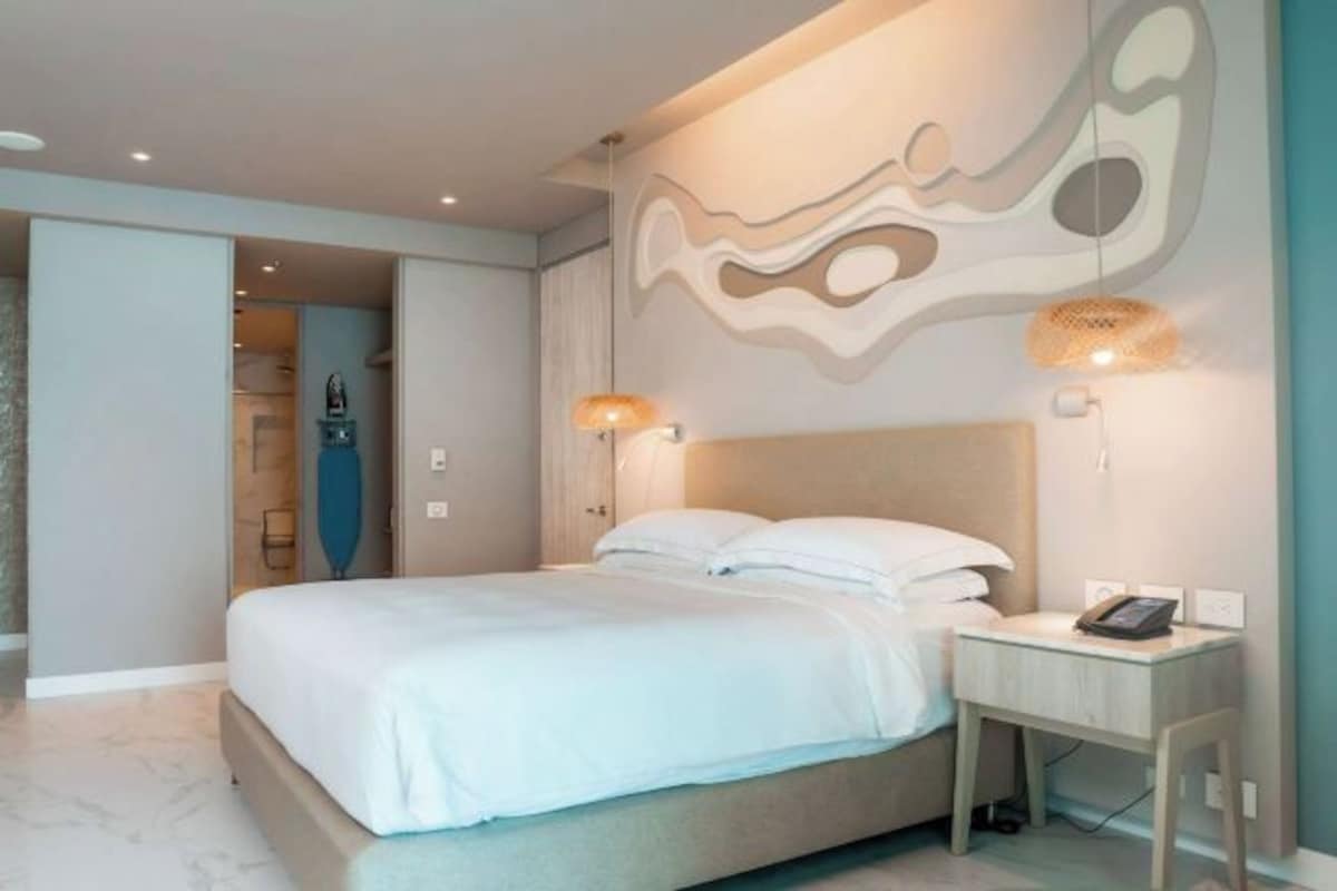 Un dormitorio moderno con una cama, lámparas de noche y una pared con arte abstracto.