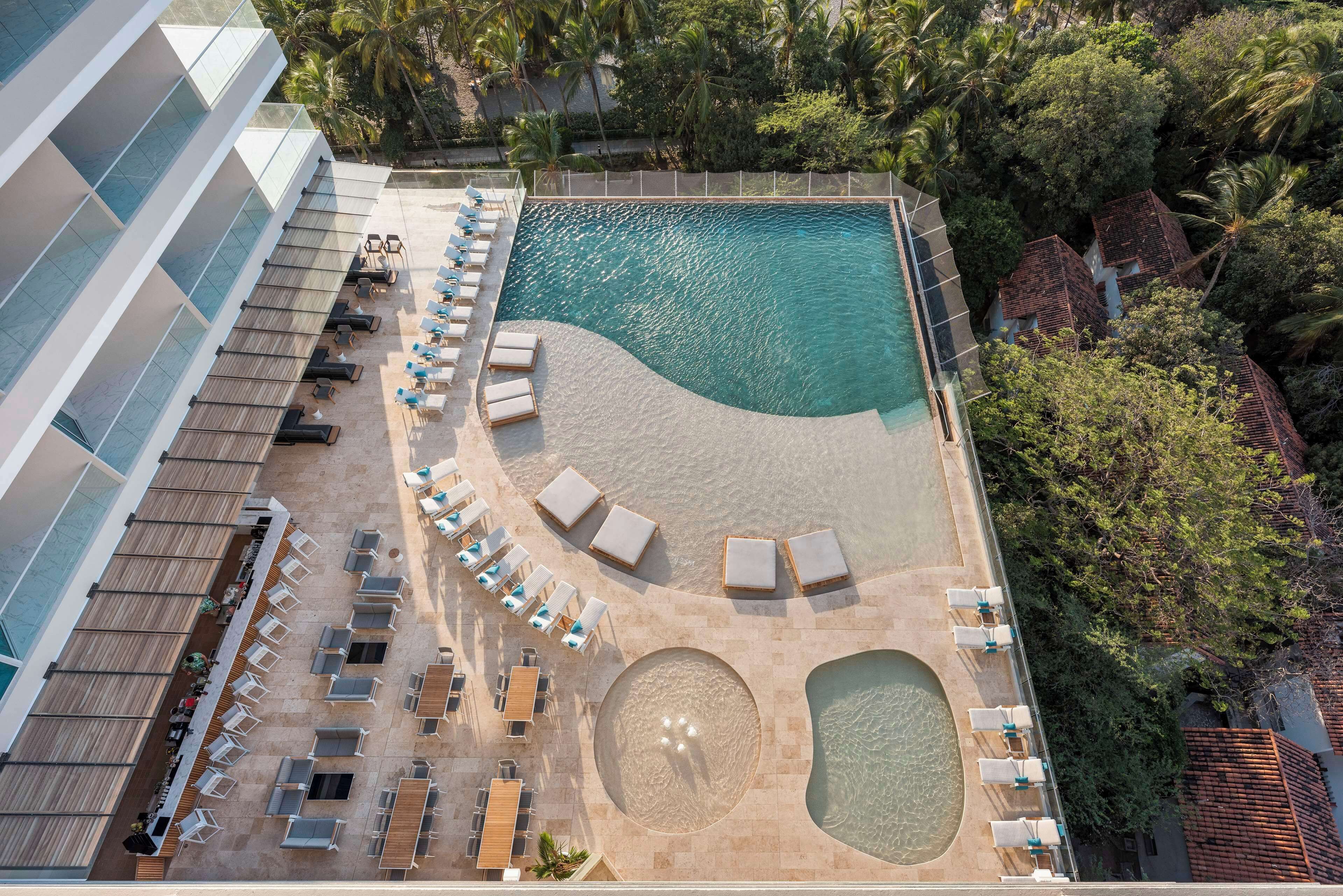 An aerial view of a resort with a swimming pool, sun loungers, and a beach area.