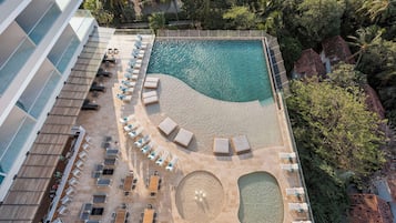 An aerial view of a resort with a swimming pool, sun loungers, and a beach area.