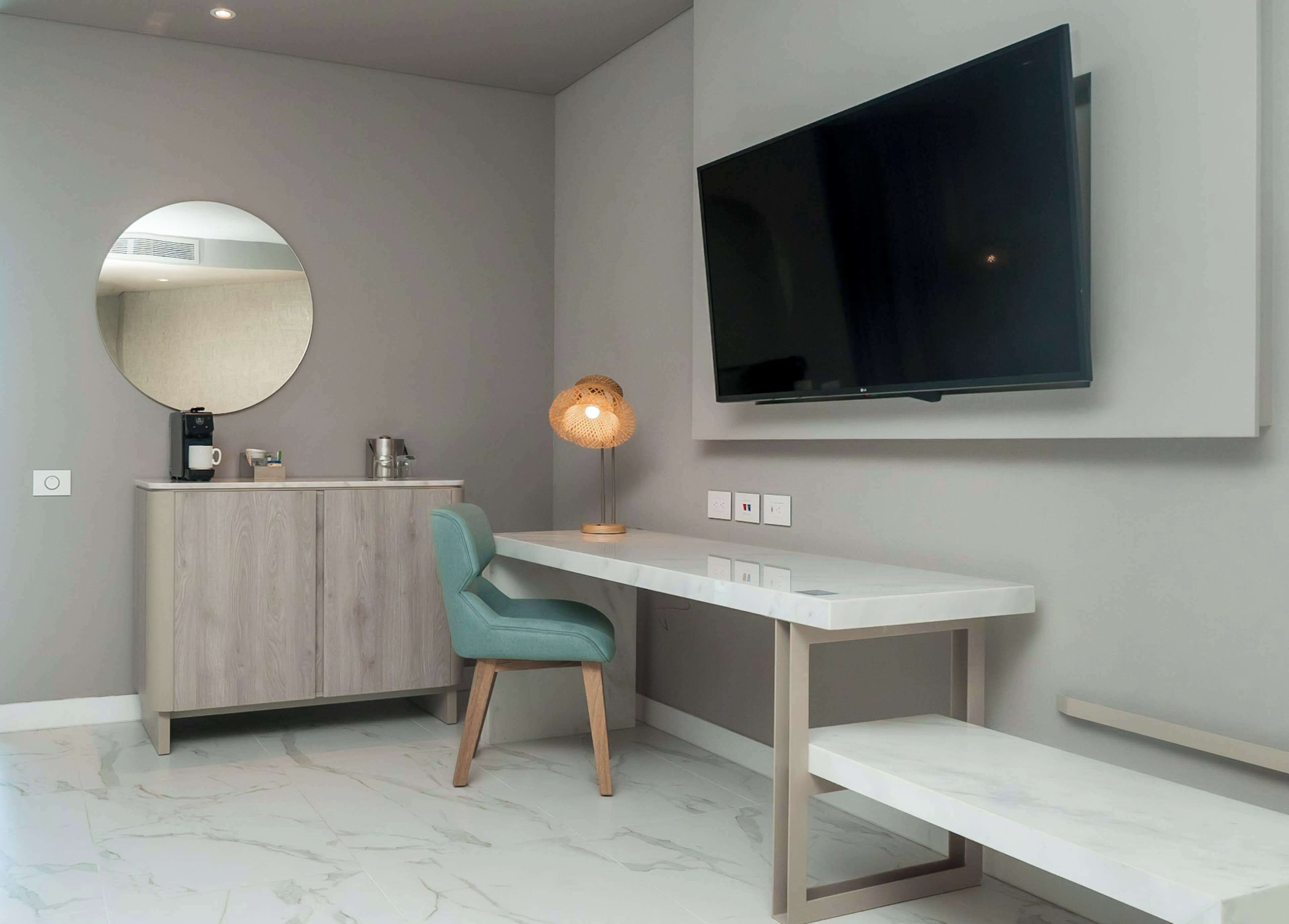 A modern room with a wooden cabinet, a teal chair, a desk, and a mounted TV.