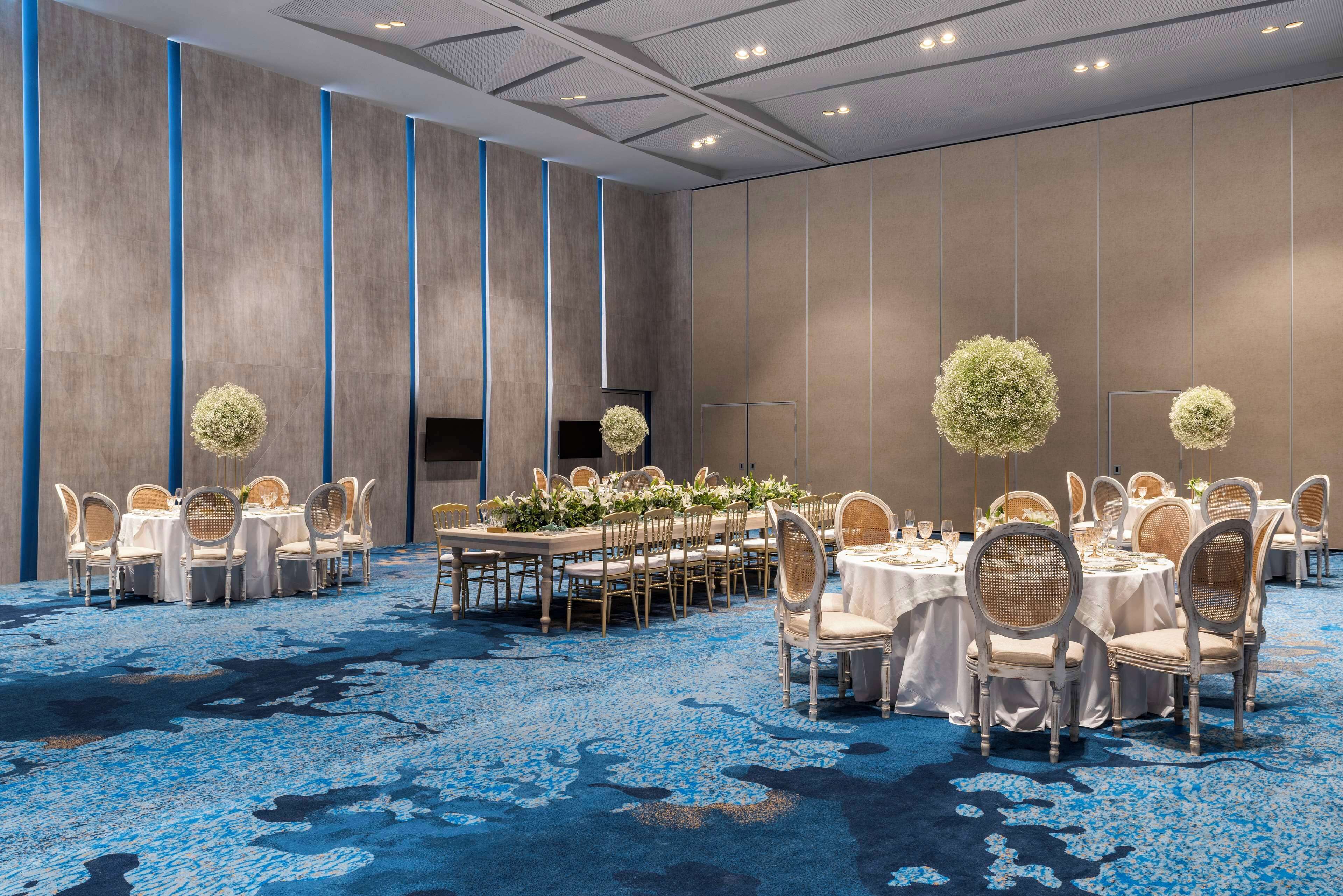 Un salón de banquetes con mesas redondas, sillas y centros de mesa florales.