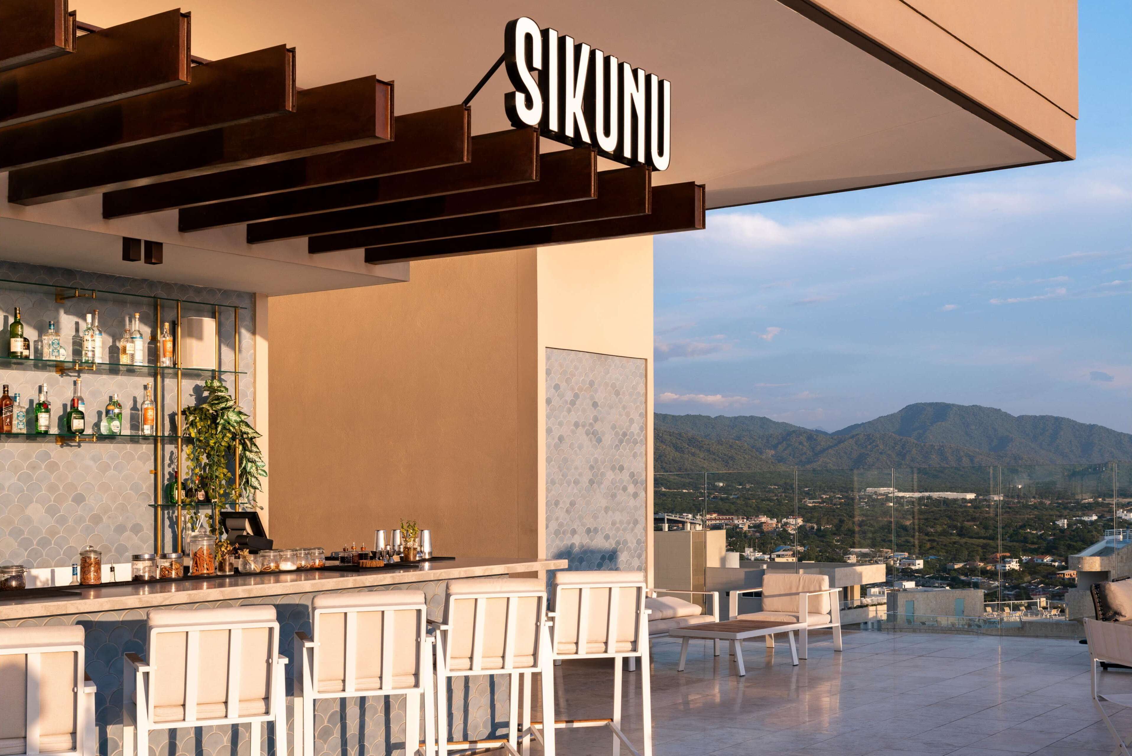 A modern bar area with a view of mountains, bar stools, and a sign that reads "SIKUNU".