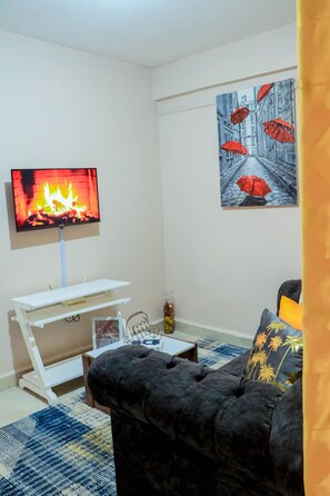 Una sala de estar con un televisor de pantalla plana montado en la pared, un sofá negro, un mueble de televisión blanco y un cuadro con sombrillas rojas en la pared.
