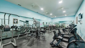 Un gimnasio con equipo de ejercicio variado, incluyendo cintas de correr y máquinas de pesas, y espejos en las paredes.