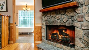Una chimenea de piedra con un televisor montado encima, un banco de madera y una ventana que da a un baño.