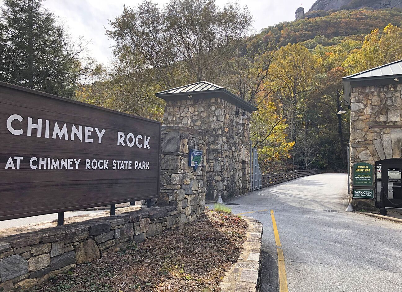 A sign for Chimney Rock State Park with a stone structure and a road leading into the park.