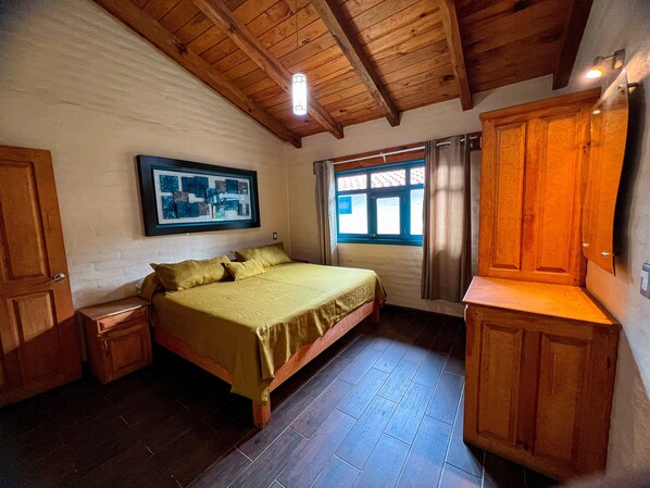 A bedroom with a bed, wooden wardrobe, a framed picture on the wall, and a window with curtains.