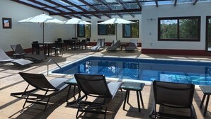 Zona de piscina con tumbonas, sombrillas y techo de cristal.