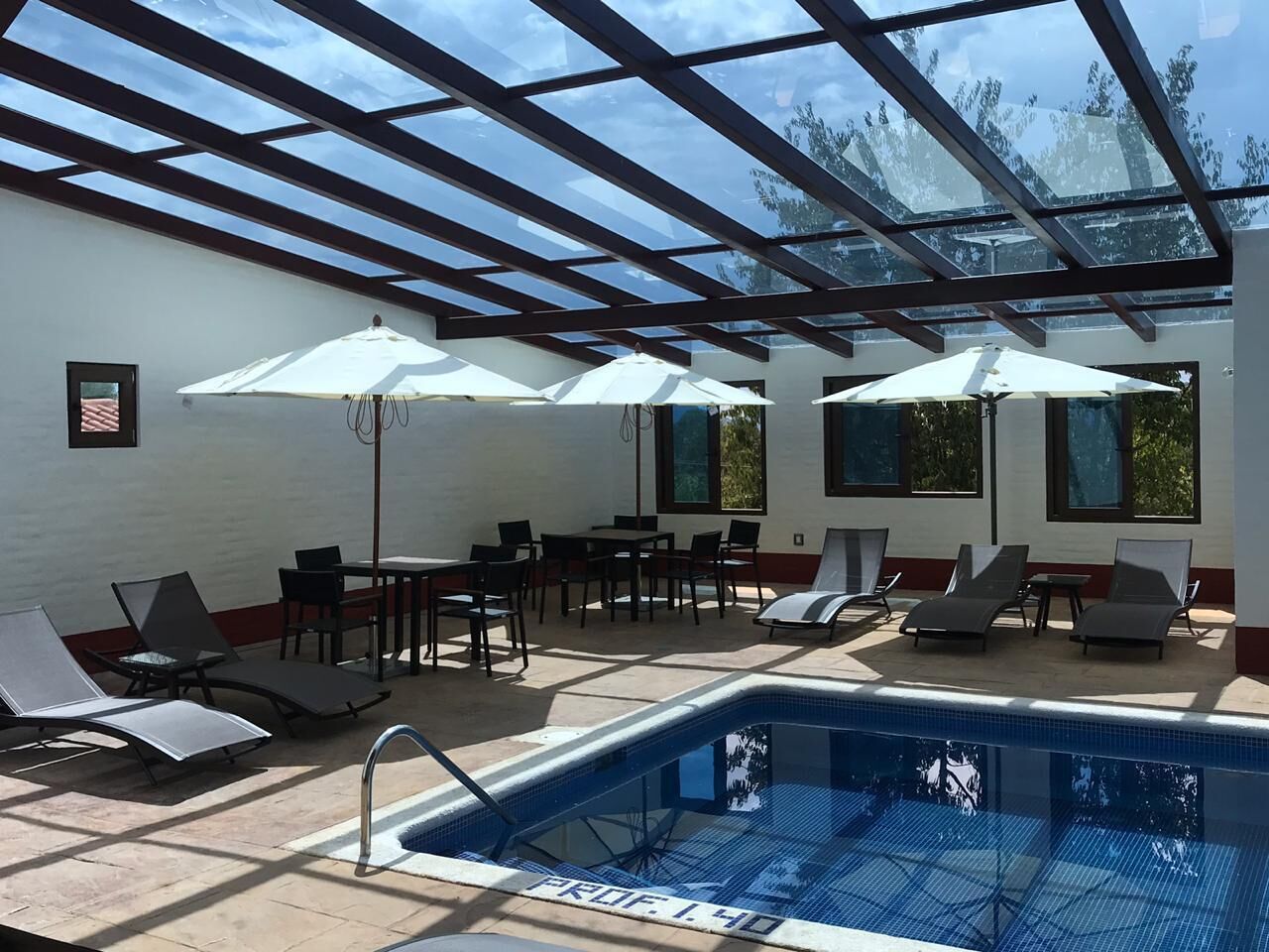 A pool area with sun loungers, umbrellas, and a glass ceiling.