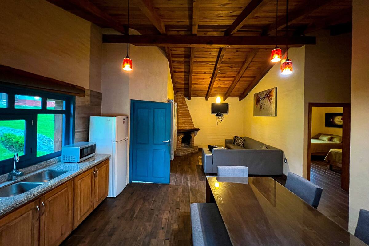 Uma cozinha compacta com pia, geladeira e uma porta azul. Há uma mesa de jantar de madeira com bancos e um sofá na sala de estar.