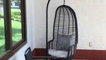 Una habitación con un sillón colgante, dos sillas, un ventanal y una pared blanca con zócalo rojo.