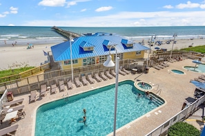 A resort with a large pool, sun loungers, and a pier extending into the ocean.