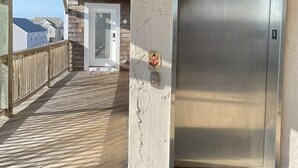 En elevator i en bygning med en træterrasse og udsigt til huse i baggrunden.