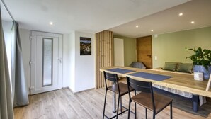 Un espace repas moderne avec une table en bois et deux tabourets de bar, une plante verte et une porte dotée de panneaux en verre dépoli.