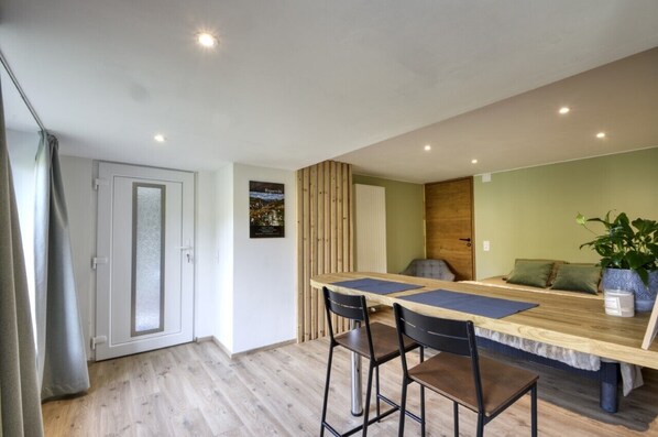 Un espace repas moderne avec une table en bois et deux tabourets de bar, une plante verte et une porte dotée de panneaux en verre dépoli.