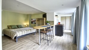 Une chambre moderne avec un lit, un bureau et une chaise. Un petit coin cuisine se trouve dans un coin de la pièce.