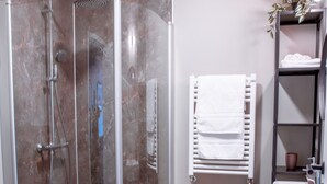 A modern bathroom with a glass-enclosed shower, a white sink, and a towel rack. - Hotel Kaldi (Dalvik)