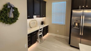 A kitchen with dark cabinets, a white countertop, a stainless steel refrigerator, and a small white chair. - Villages, 3bed- 2.5ba waterfrnt+ golf cart- all bedrooms have king beds! (Wildwood)