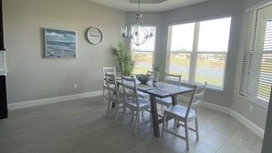 A spacious dining area with a high ceiling, a chandelier, a clock, and a view through large windows. - Villages, 3bed- 2.5ba waterfrnt+ golf cart- all bedrooms have king beds! (Wildwood)