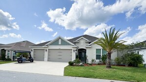 A single-story house with a garage, a driveway, and a well-maintained lawn. - Villages, 3bed- 2.5ba waterfrnt+ golf cart- all bedrooms have king beds! (Wildwood)