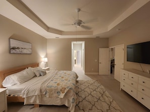 A bedroom with a bed, bedside table, lamp, TV, and a ceiling fan.