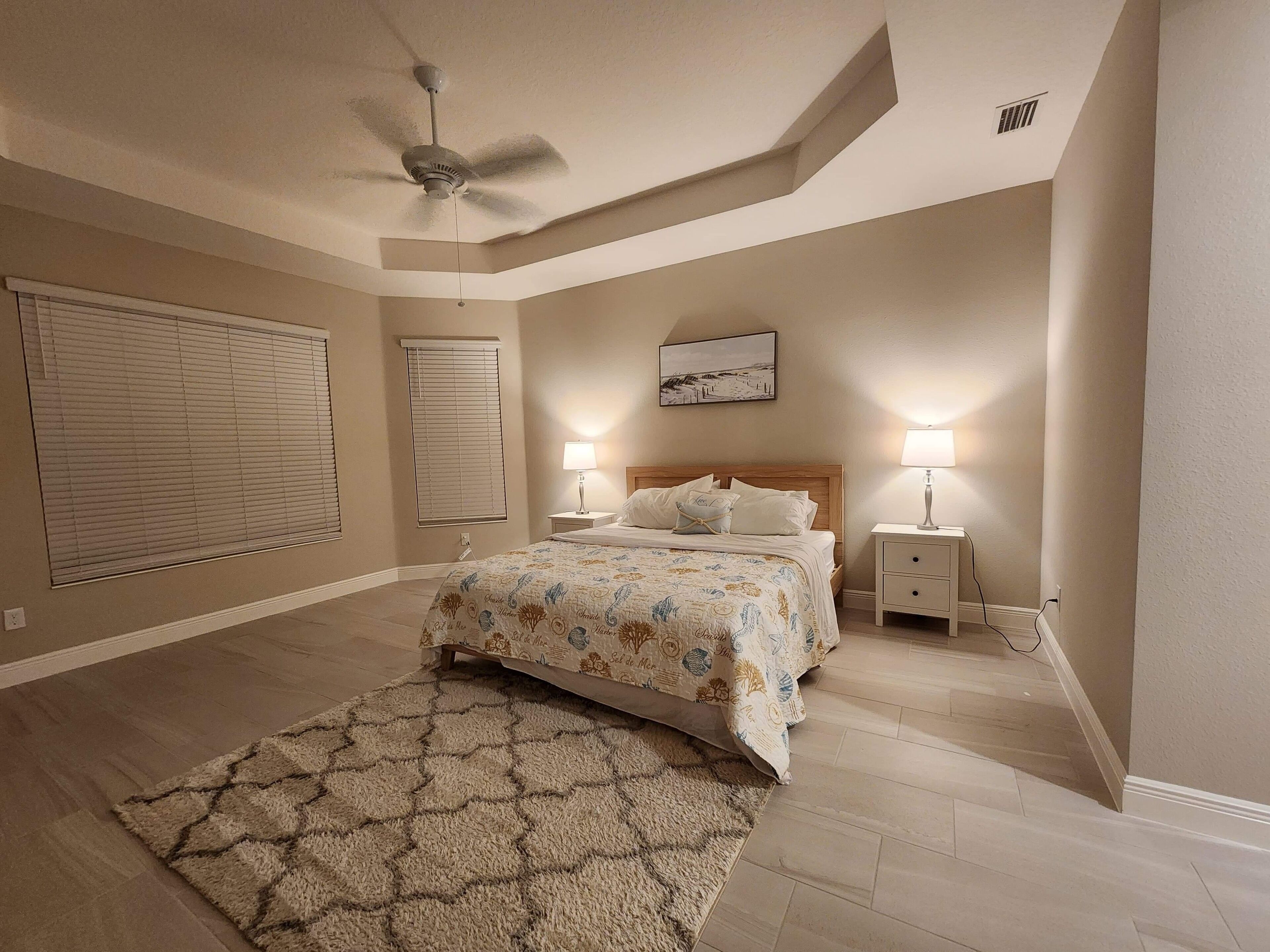 A bedroom with a bed, two bedside tables with lamps, a ceiling fan, and a rug.