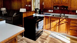 A kitchen with wooden cabinets, a black stove, and a dining area with stools. - Lakefront year round home, gorgeous views, central location (Remsen)
