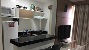A compact kitchen with a black countertop, white chairs, a TV, and a microwave. - Rio Quente - Hotel Veredas do Rio Quente - Apartment for Rent (Rio Quente - Esplanada do Rio Quente)