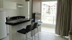 A modern kitchen with a bar area, a refrigerator, and a window with curtains. - Rio Quente - Hotel Veredas do Rio Quente - Apartment for Rent (Rio Quente - Esplanada do Rio Quente)