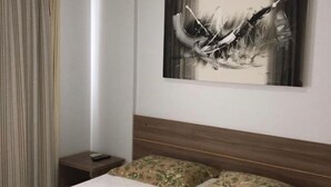 A hotel room with a bed, a nightstand, a painting on the wall, and a window with curtains. - Rio Quente - Hotel Veredas do Rio Quente - Apartment for Rent (Rio Quente - Esplanada do Rio Quente)
