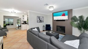 Una sala de estar moderna con un sofá seccional gris, un televisor de pantalla plana montado en la pared, una chimenea y un ventanal con vistas al exterior.