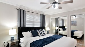 Un dormitorio moderno con una cama grande, dos mesitas de noche con lámparas, un ventilador de techo y un espejo amplio.
