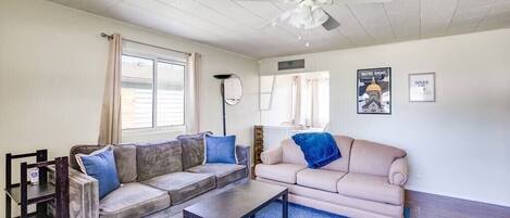 Un salon avec un canapé beige, une table basse, un ventilateur de plafond et une fenêtre avec des rideaux.