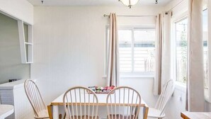 Ein Essbereich mit einem Holztisch, vier Stühlen, einem Fenster mit Vorhängen und einer weißen Wand.